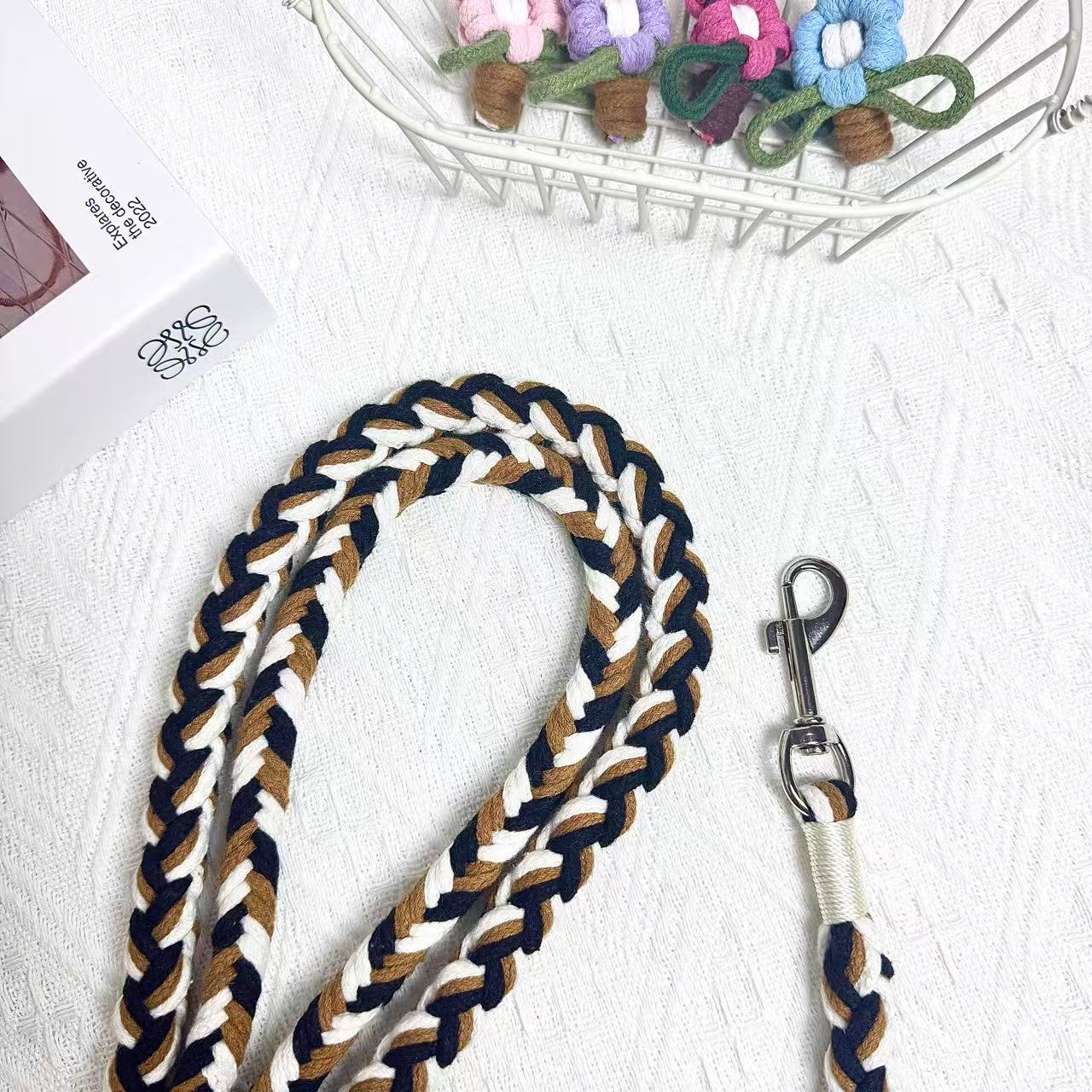 A close-up of a black, brown, and white handwoven dog leash, showcasing the durable braided design and a polished metal clip for secure attachment.