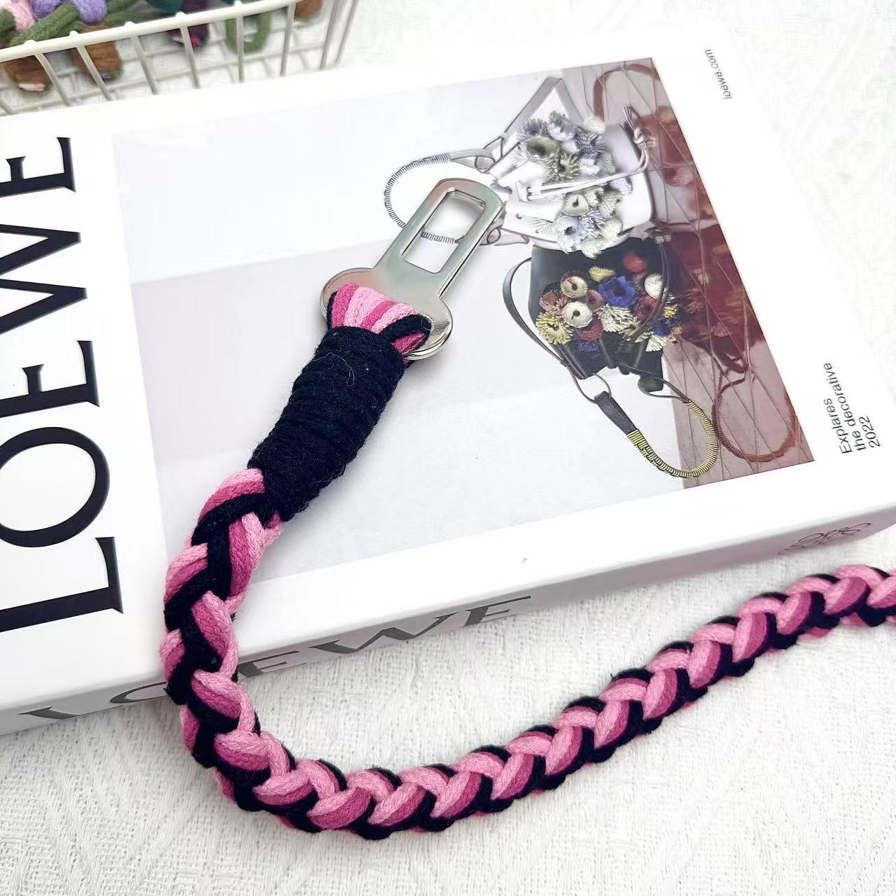 A handcrafted dog seatbelt attachment featuring a braided rope design in pink and black. The sturdy metal clip is securely wrapped with black cord, ensuring durability.