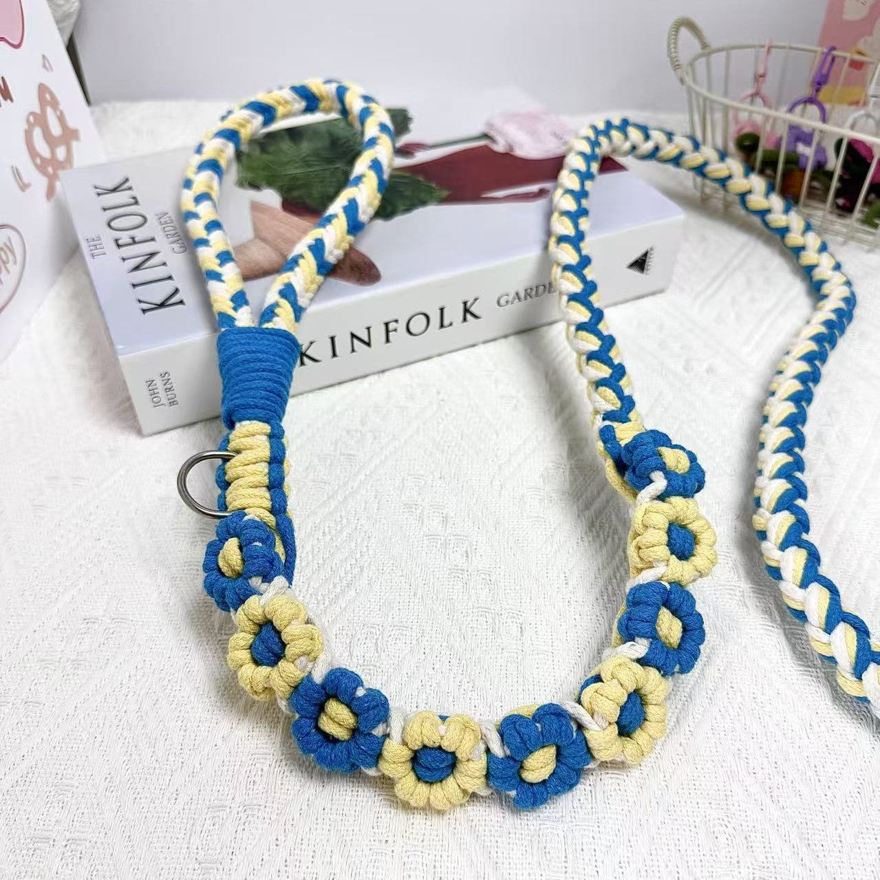 A detailed view of a blue and yellow handwoven dog leash with a charming floral design. The leash is elegantly placed on a textured white surface, highlighting its intricate craftsmanship and vibrant colors.