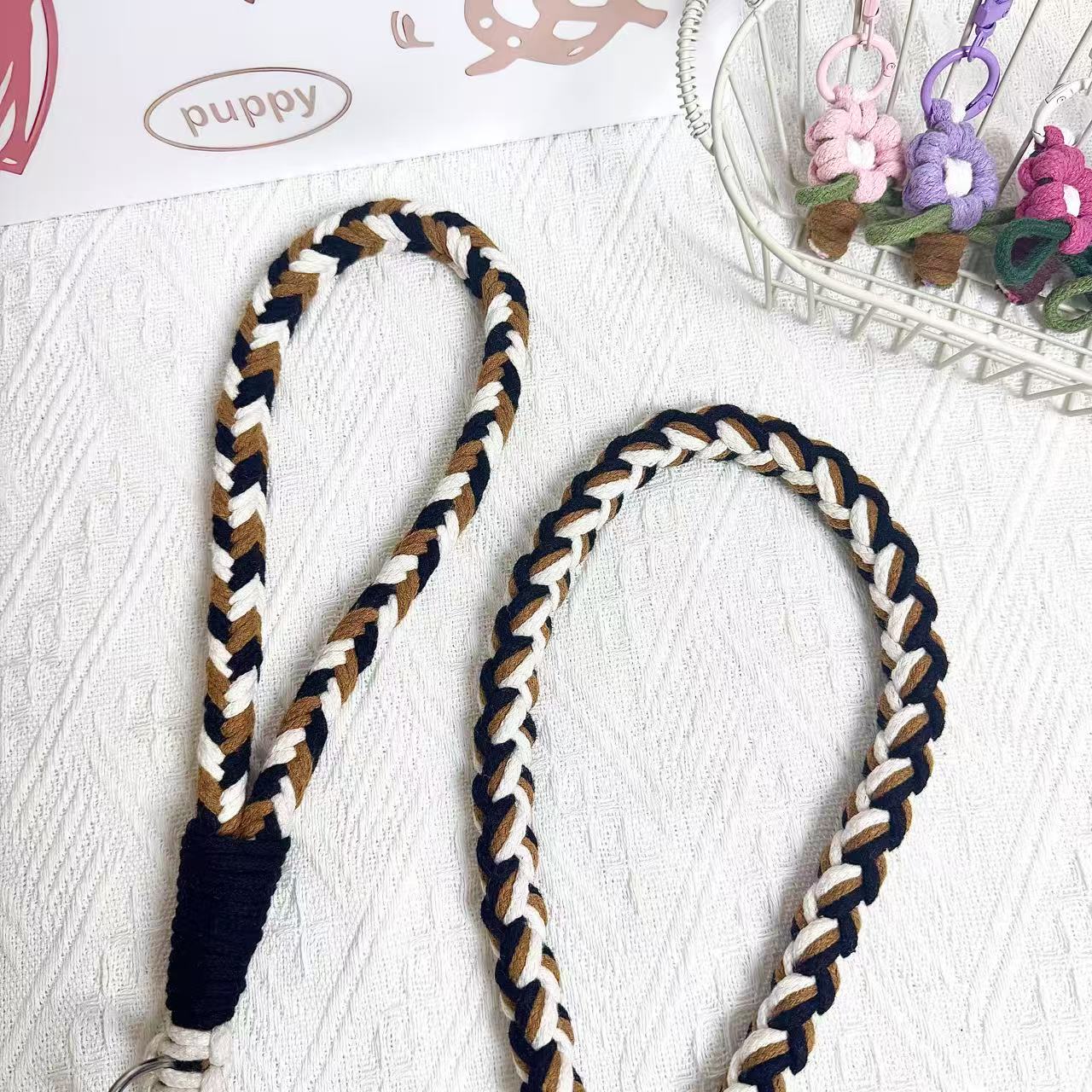 A detailed view of a black, brown, and white braided dog leash, highlighting its sturdy handwoven handle section and the neatly arranged leash cord.