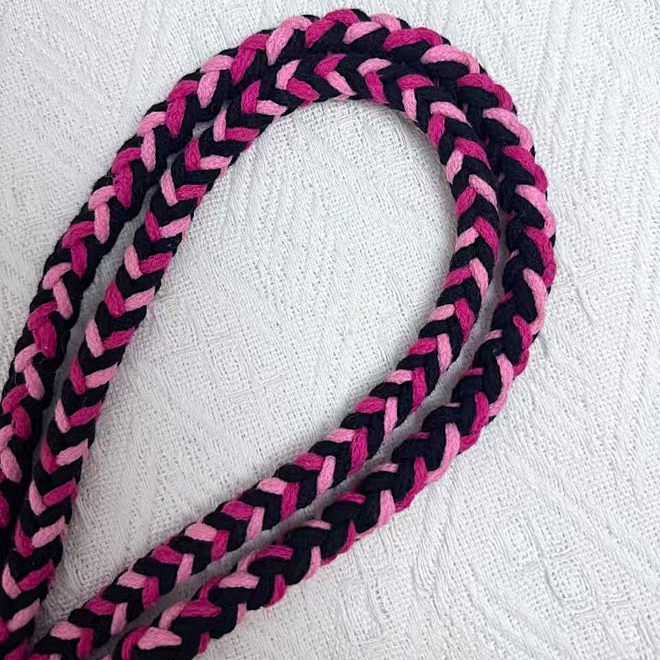 A detailed view of a black and pink braided dog leash, highlighting its sturdy handwoven handle section and the neatly arranged leash cord.