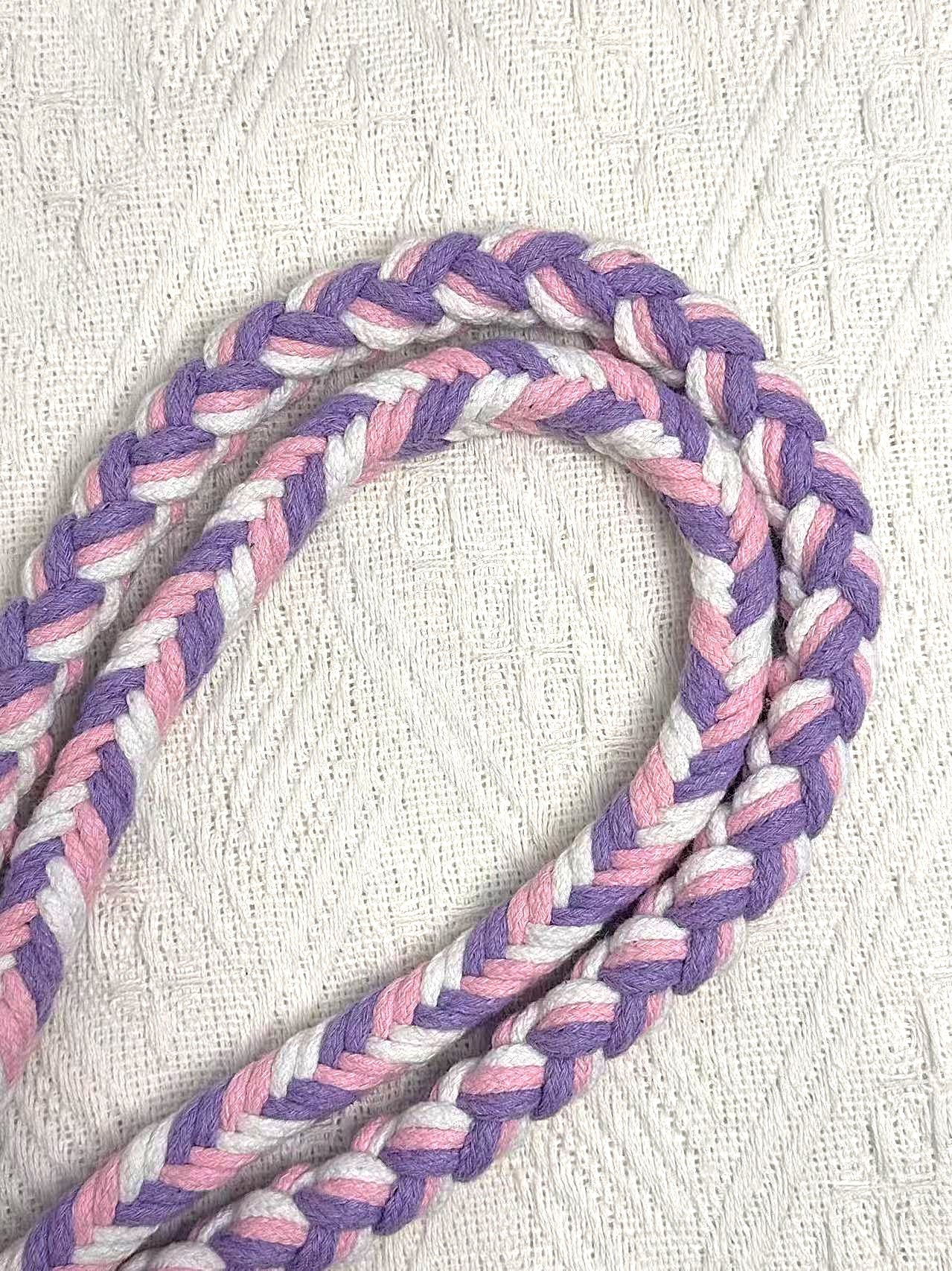 A detailed view of a pink, purple, and white braided dog leash, highlighting its sturdy handwoven handle section and the neatly arranged leash cord.