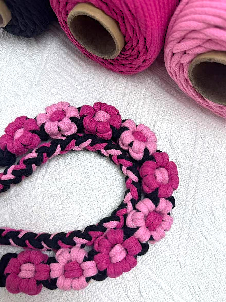 Dog leash decorated with numerous handcrafted flowers in eye-catching black and pink tones, surrounded by matching black and pink rope roll.