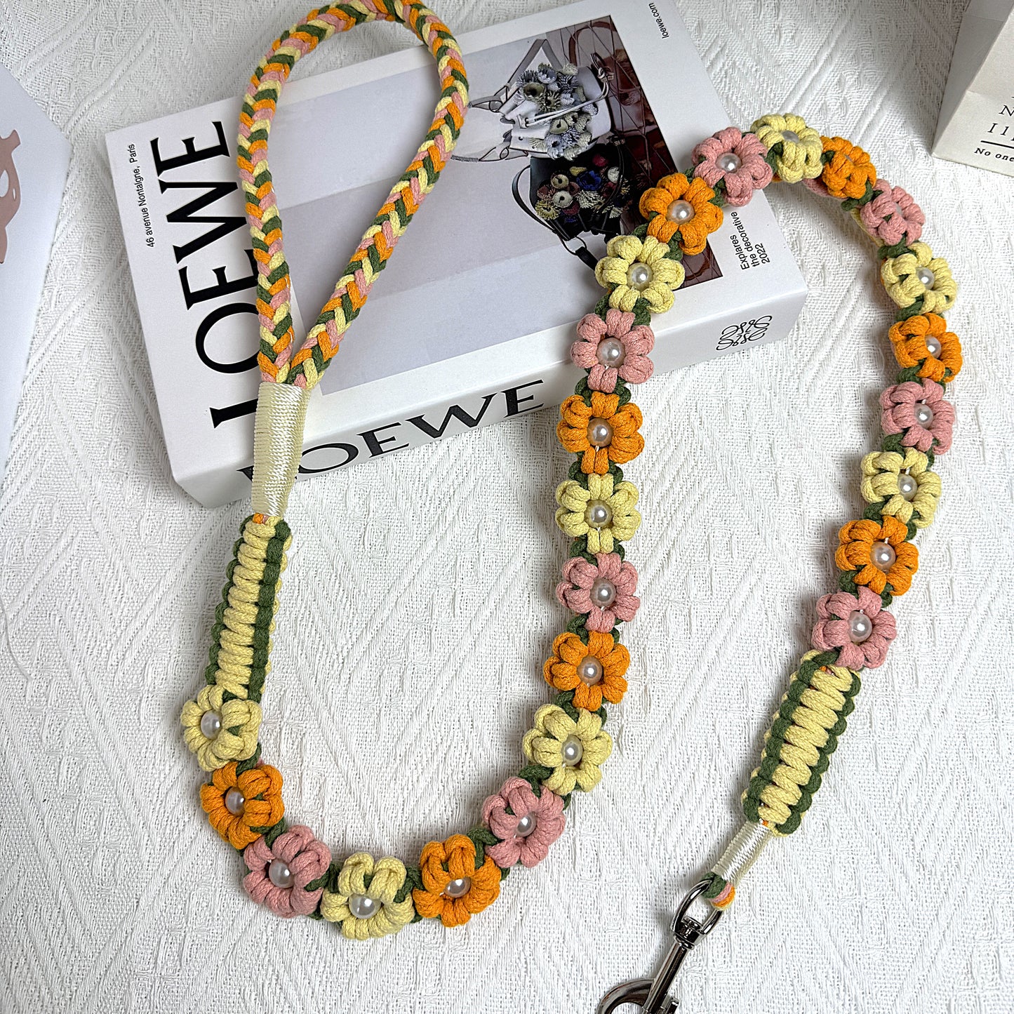 The soft handle and the clip of the handmade orange, yellow and pink dog leash, featuring multiple beautiful woven flowers.