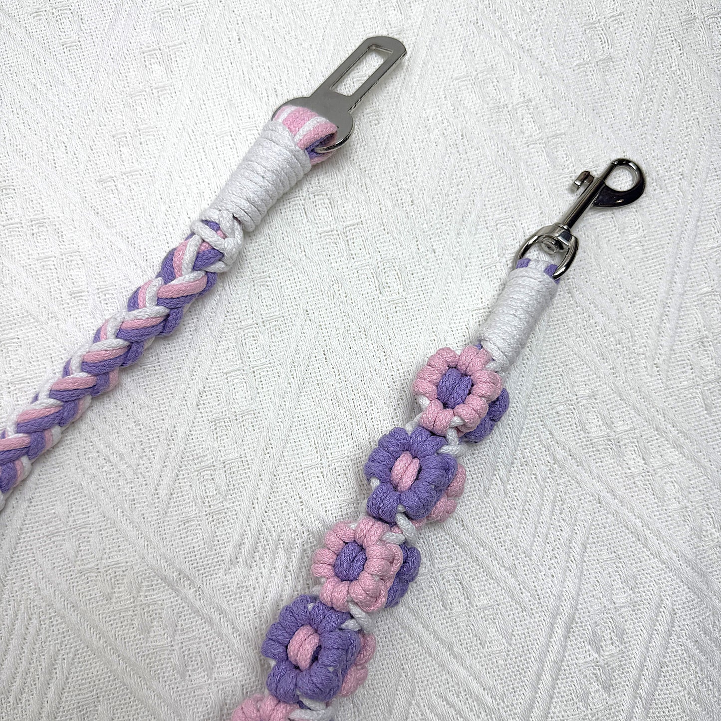 The sturdy metal clip and attachment of the pink and purple dog seatbelt, decorated with numerous handcrafted flowers.