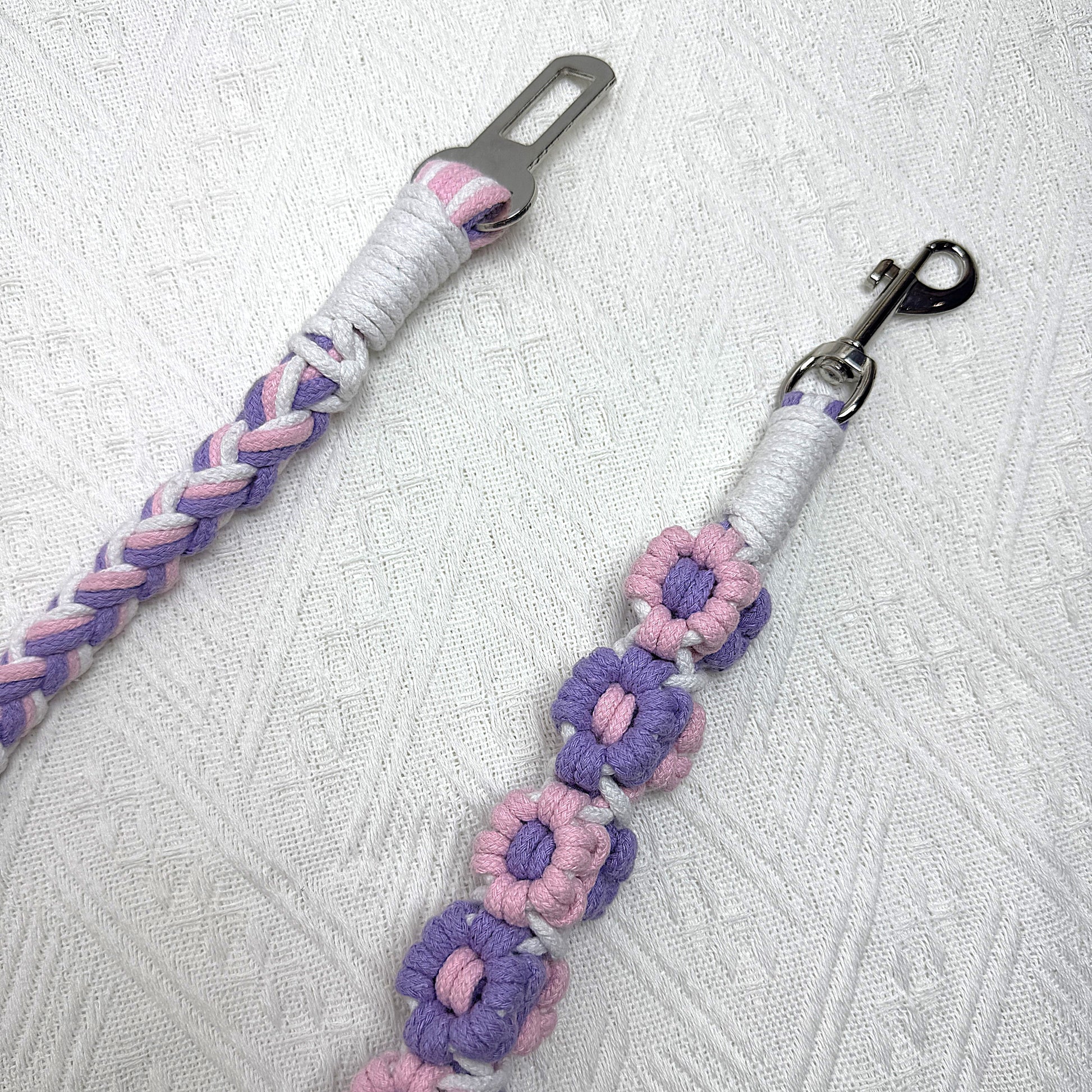 The sturdy metal clip and attachment of the pink and purple dog seatbelt, decorated with numerous handcrafted flowers.