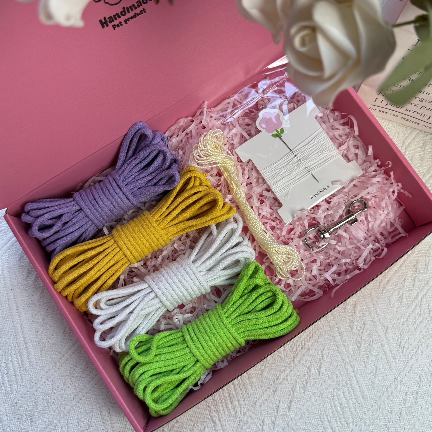DIY dog leash kit featuring green, purple, and yellow cotton ropes, ice silk cord, one sewing kit, and a stainless steel clasp, neatly arranged in a pink box with decorative shredded paper.