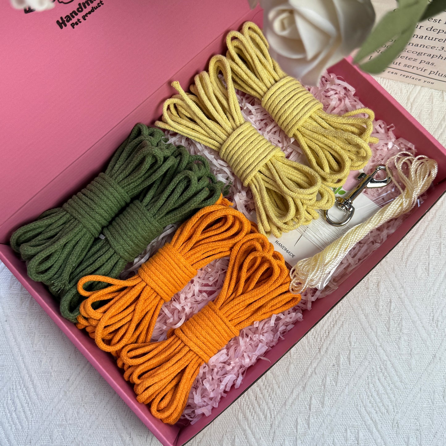 DIY dog leash kit featuring green, orange, and yellow cotton ropes, ice silk cord, one sewing kit, and a stainless steel clasp, neatly arranged in a pink box with decorative shredded paper.