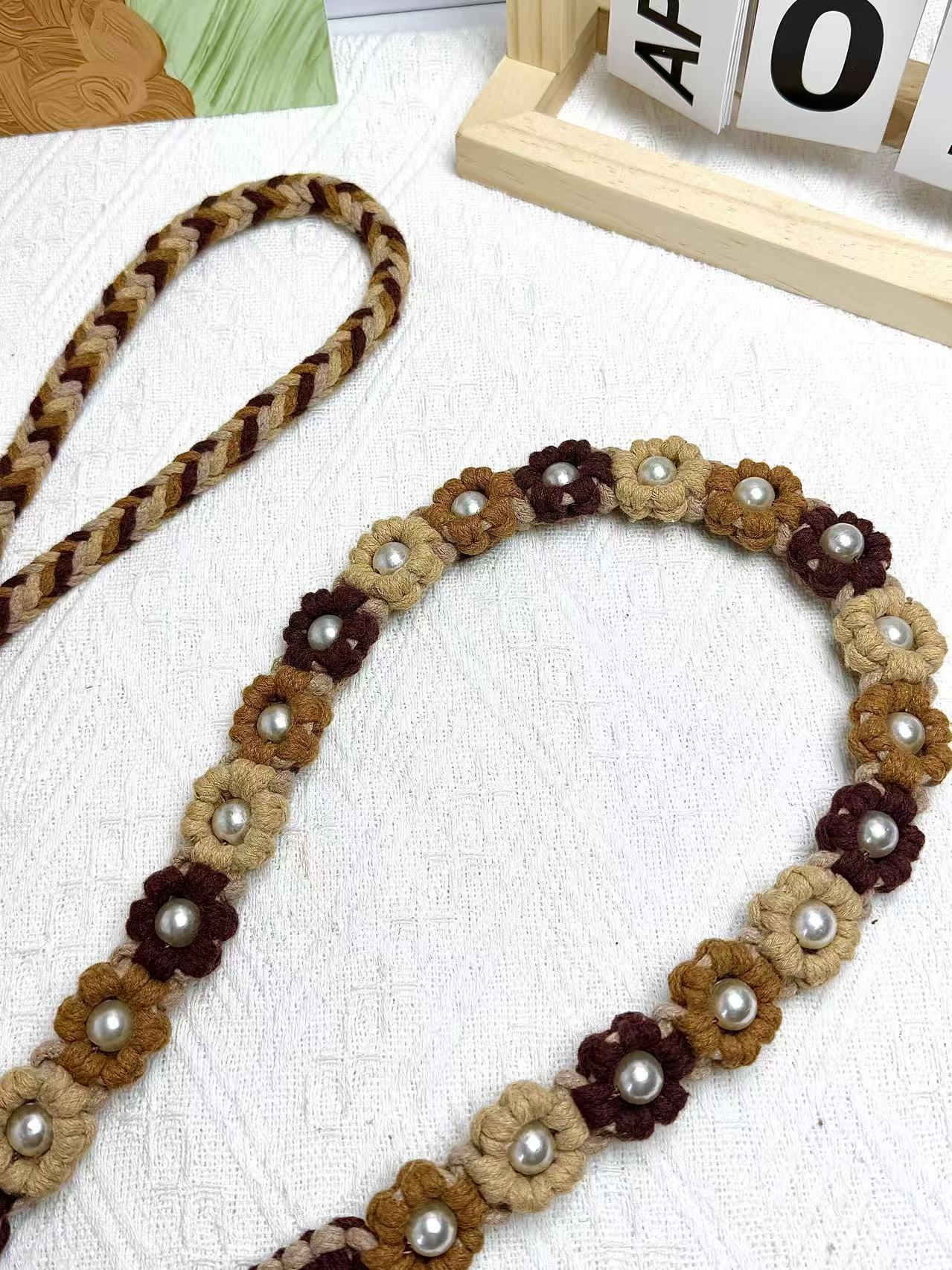 A detailed view of a gradient brown handwoven dog leash with a charming floral design. The leash is elegantly placed on a textured white surface, highlighting its intricate craftsmanship and vibrant colors.