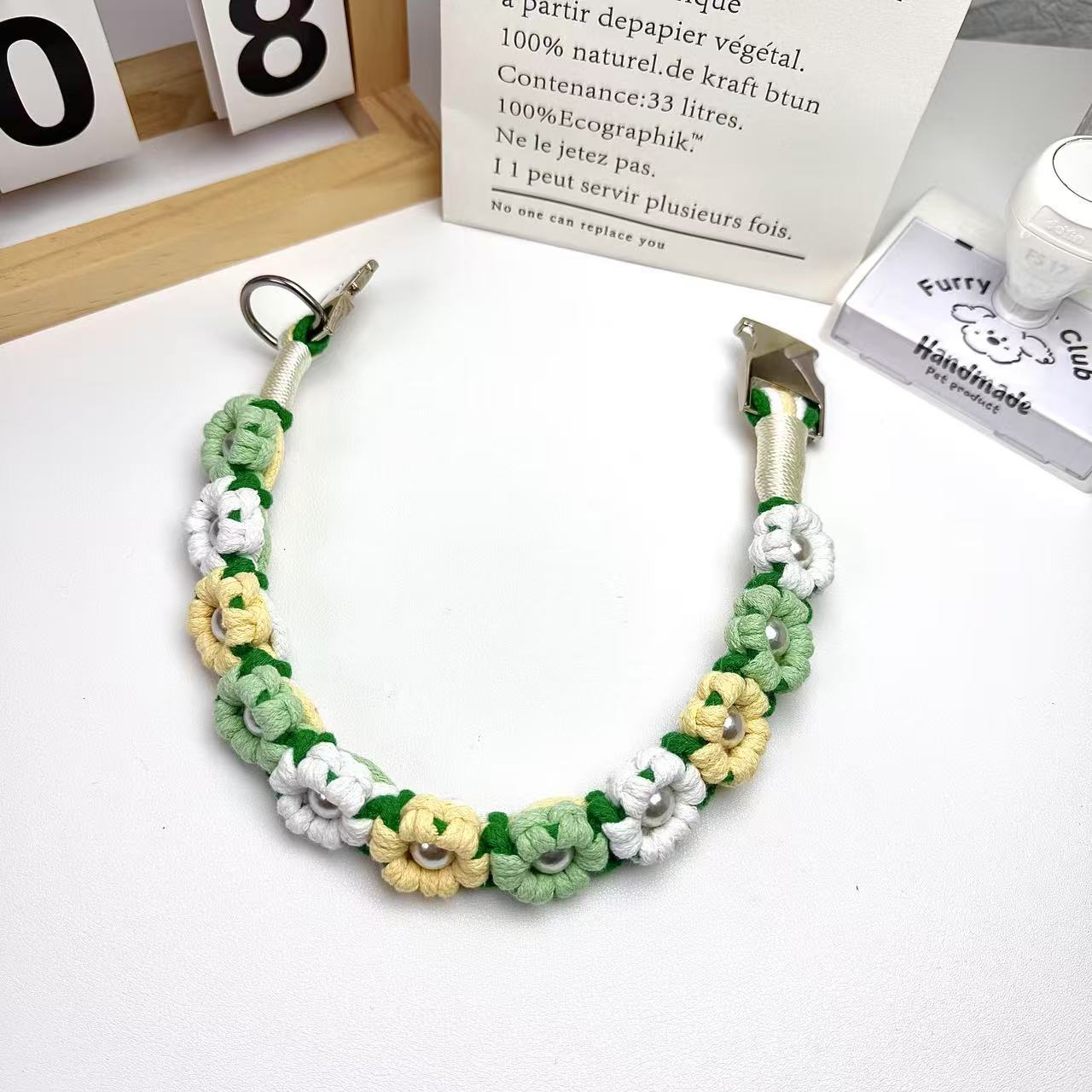 Handwoven dog collar with colorful flowers and pearl accents, featuring a stainless steel clasp and D-ring, on a white fabric background.