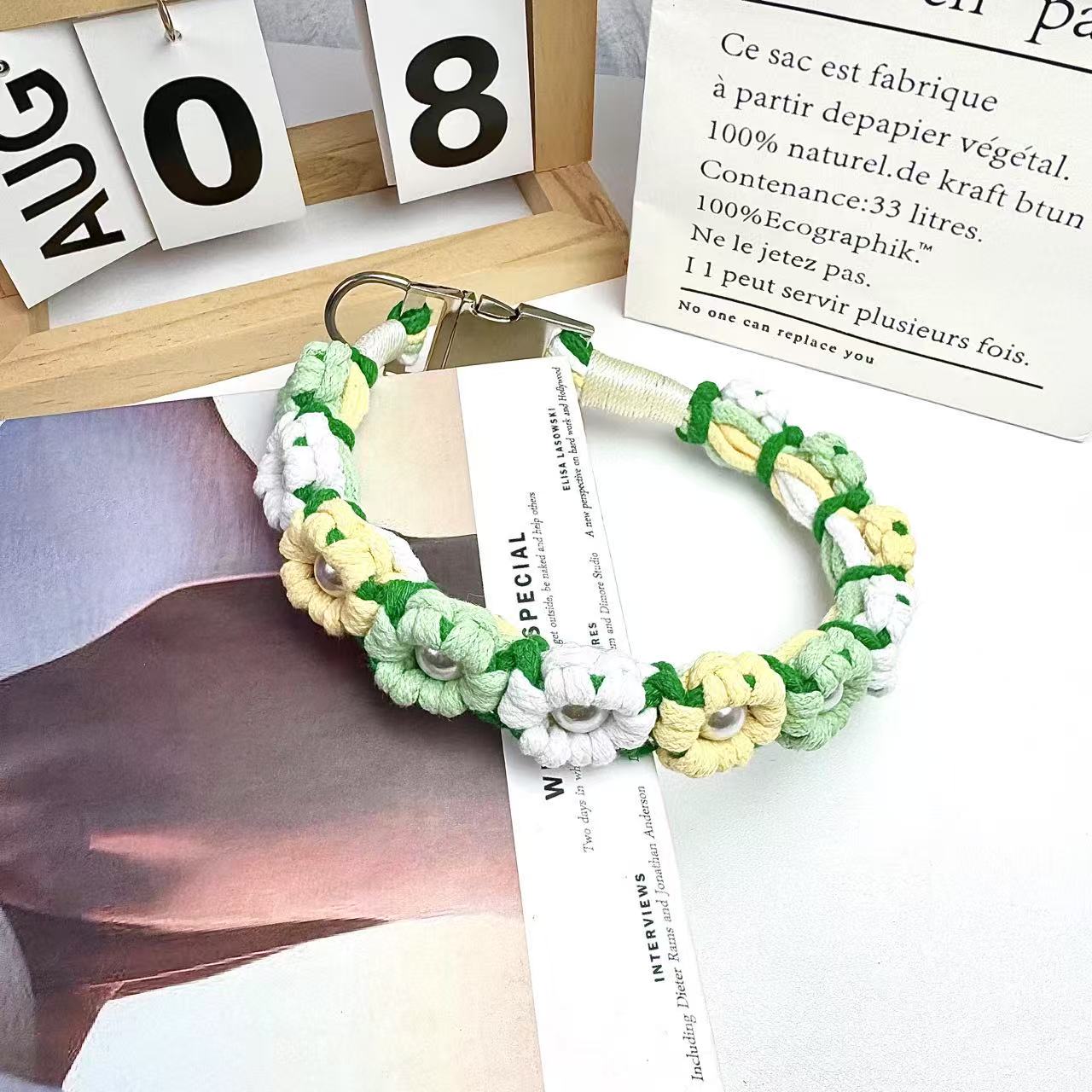 A vibrant handwoven dog collar featuring colorful floral designs with pearl accents at the center of each flower. The collar includes a stainless steel clasp, set against a cozy background with decorative elements.
