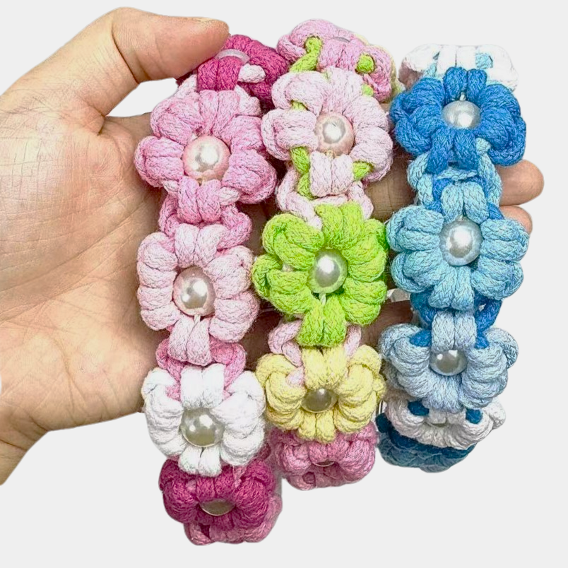 A hand holding three handmade dog collars in pink, green, and blue color themes, showcasing braided flower patterns with pearl, highlighting the lightweight and stylish design.