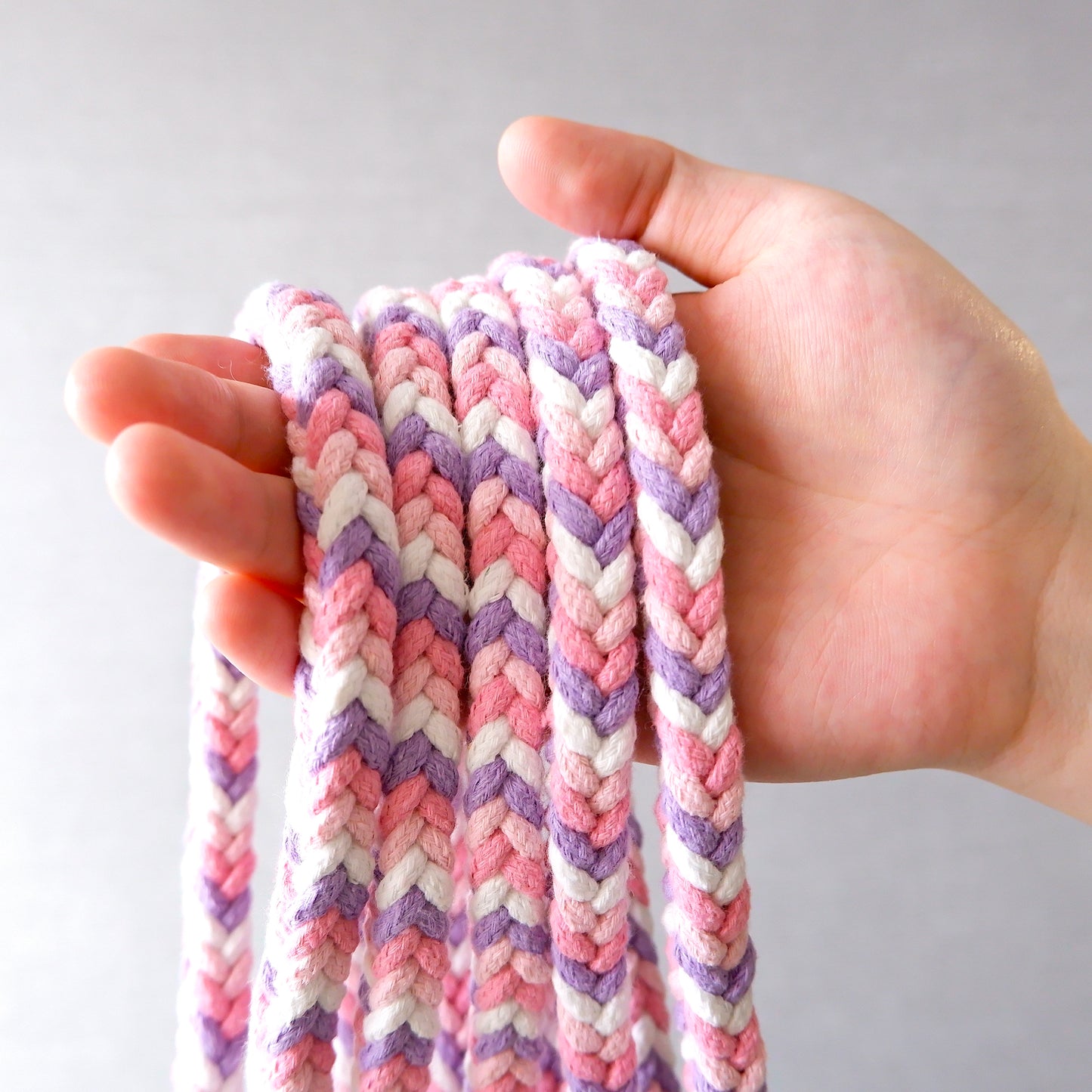 A hand holding multiple handmade dog leash segments in purple and pink, highlighting the unique design.