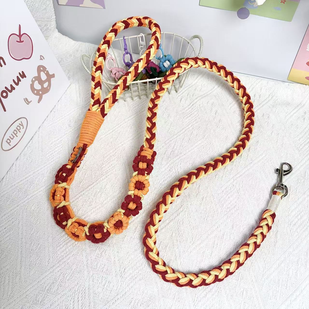 A beautifully handwoven orange and red dog leash featuring a sturdy loop handle and a metal clip for secure attachment, displayed on a white surface with decorative elements.