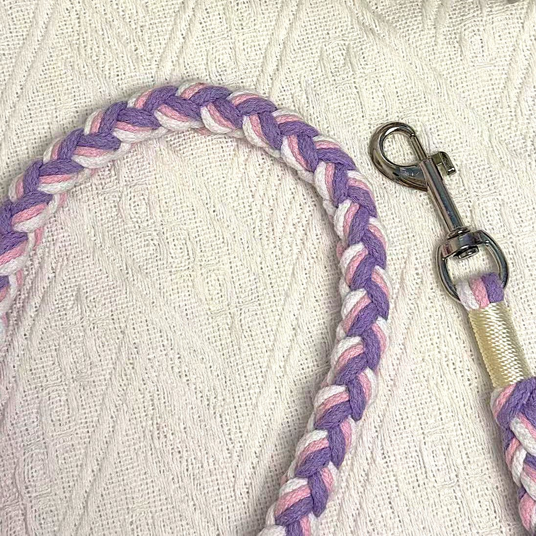 A close-up of a pink, purple, and white handwoven dog leash, showcasing the durable braided design and a polished metal clip for secure attachment.