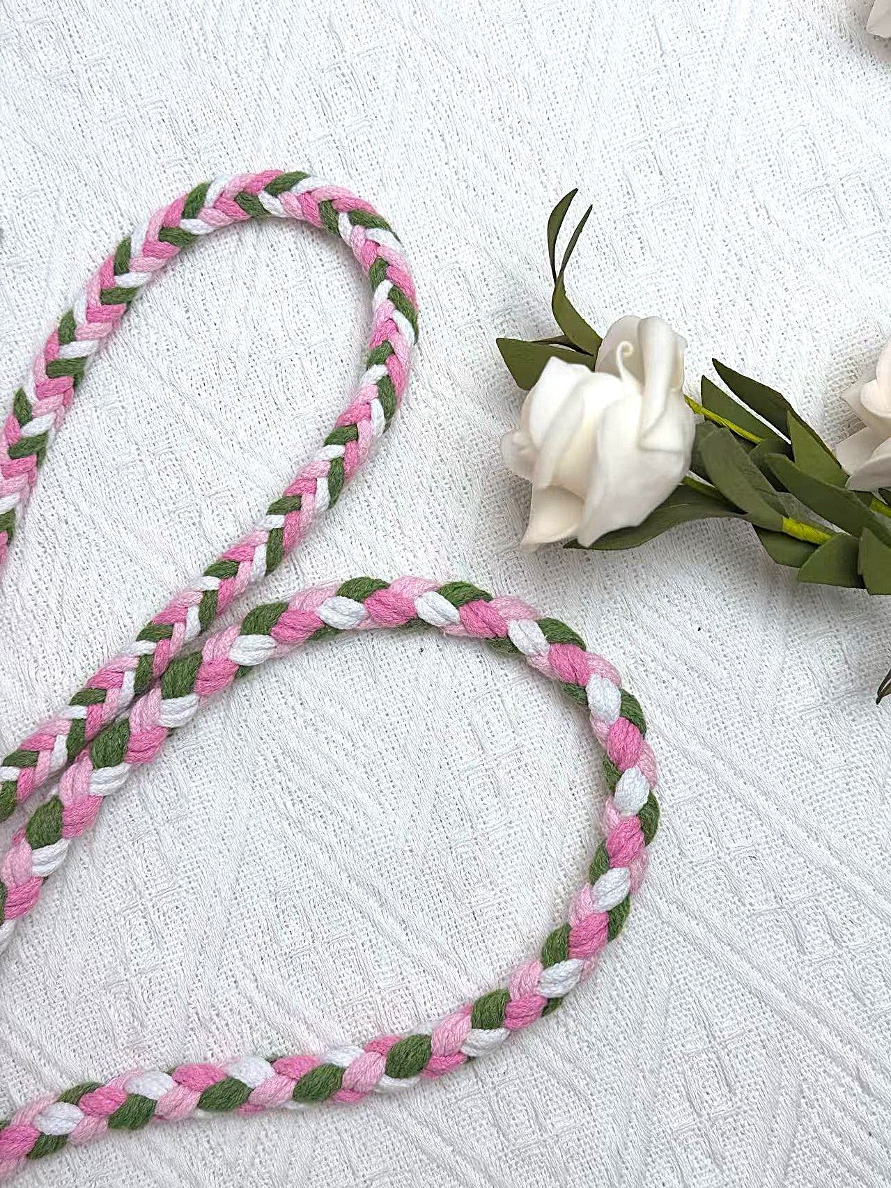 A close-up of a handwoven pink, green and white braided rope, crafted from soft cotton material and decorated with white flowers, it creates an elegant feeling.