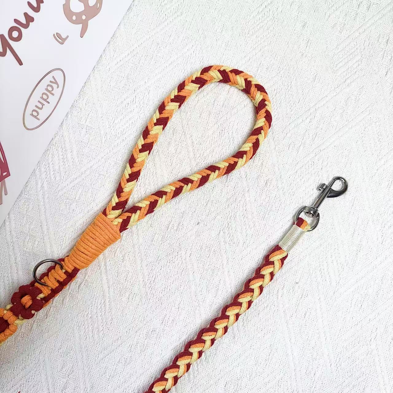 A close-up of an orange, red and yellow handwoven dog leash, showcasing the durable soft handle and a polished metal clip for secure attachment.