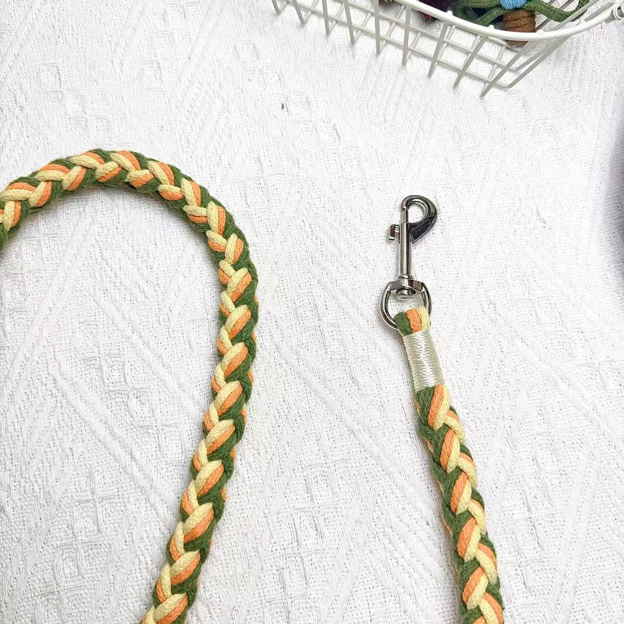 A close-up of an orange, yellow, and green handwoven dog leash, showcasing the durable braided design and a polished metal clip for secure attachment.