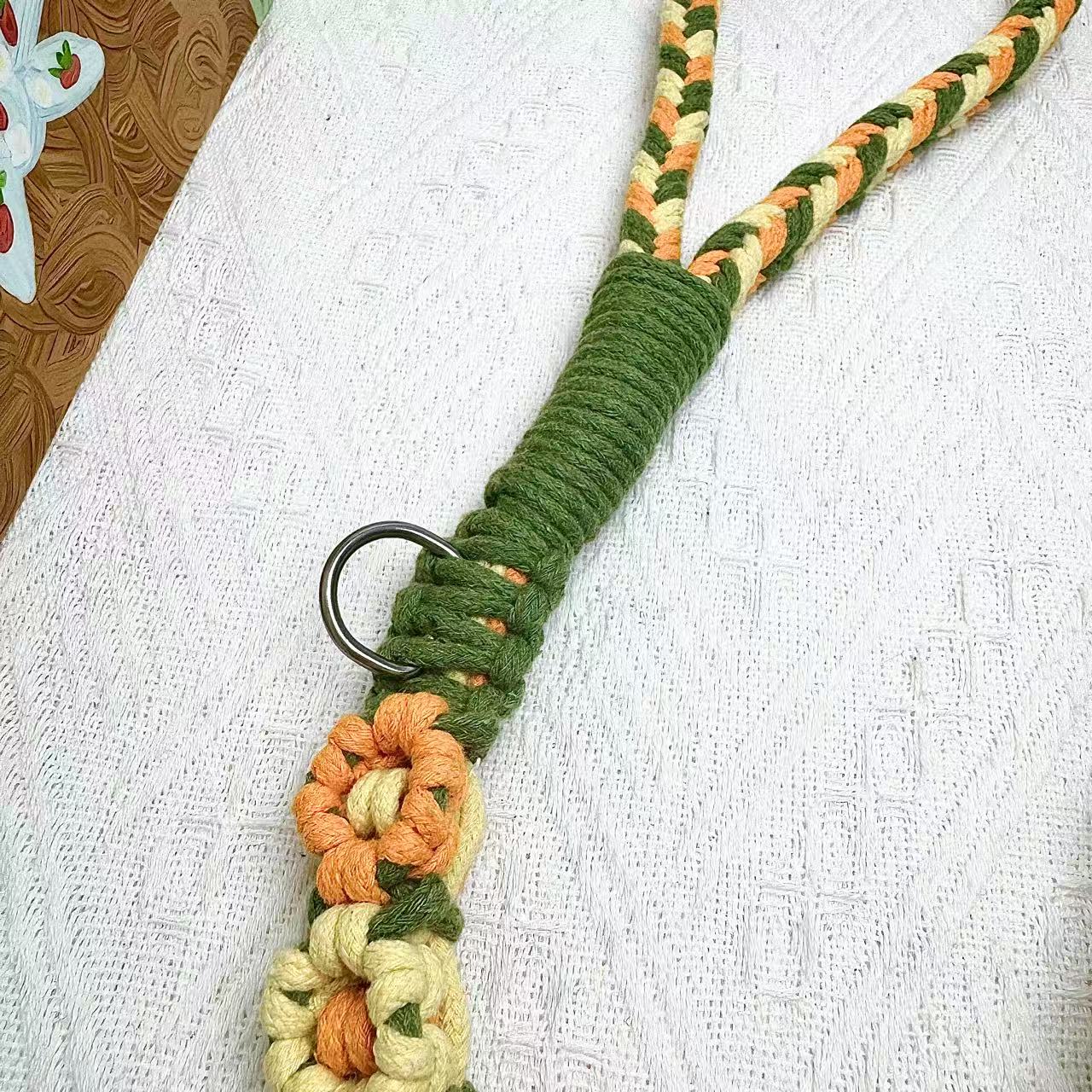 A detailed view of an orange and yellow handwoven dog leash with a charming floral design. The leash is elegantly placed on a textured white surface, highlighting its intricate craftsmanship and vibrant colors.