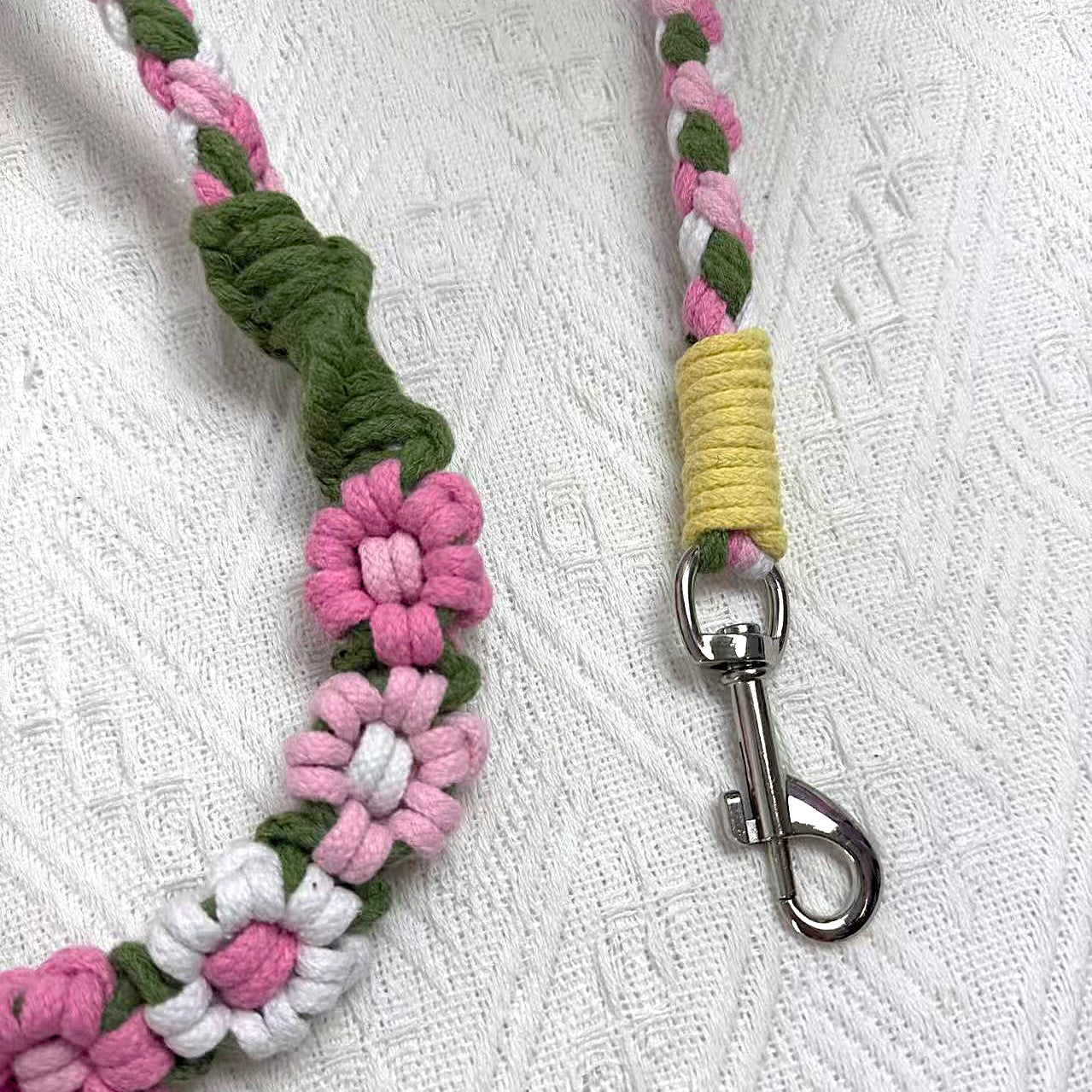 A close-up of a pink, green, and white handwoven dog leash, showcasing the fashion braided floral design and a polished metal clip for secure attachment.