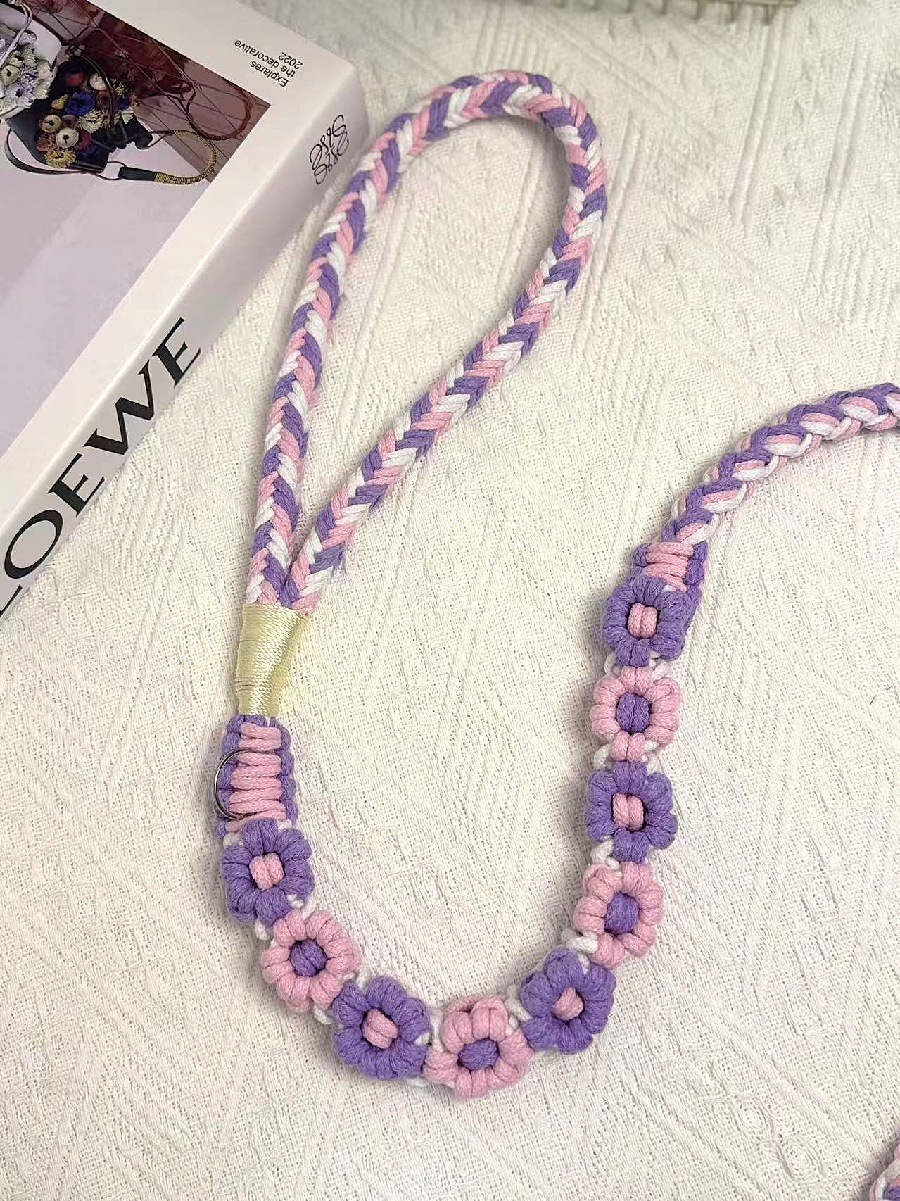 A detailed view of a purple and pink handwoven dog leash with a charming floral design. The leash is elegantly placed on a textured white surface, highlighting its intricate craftsmanship and vibrant colors.