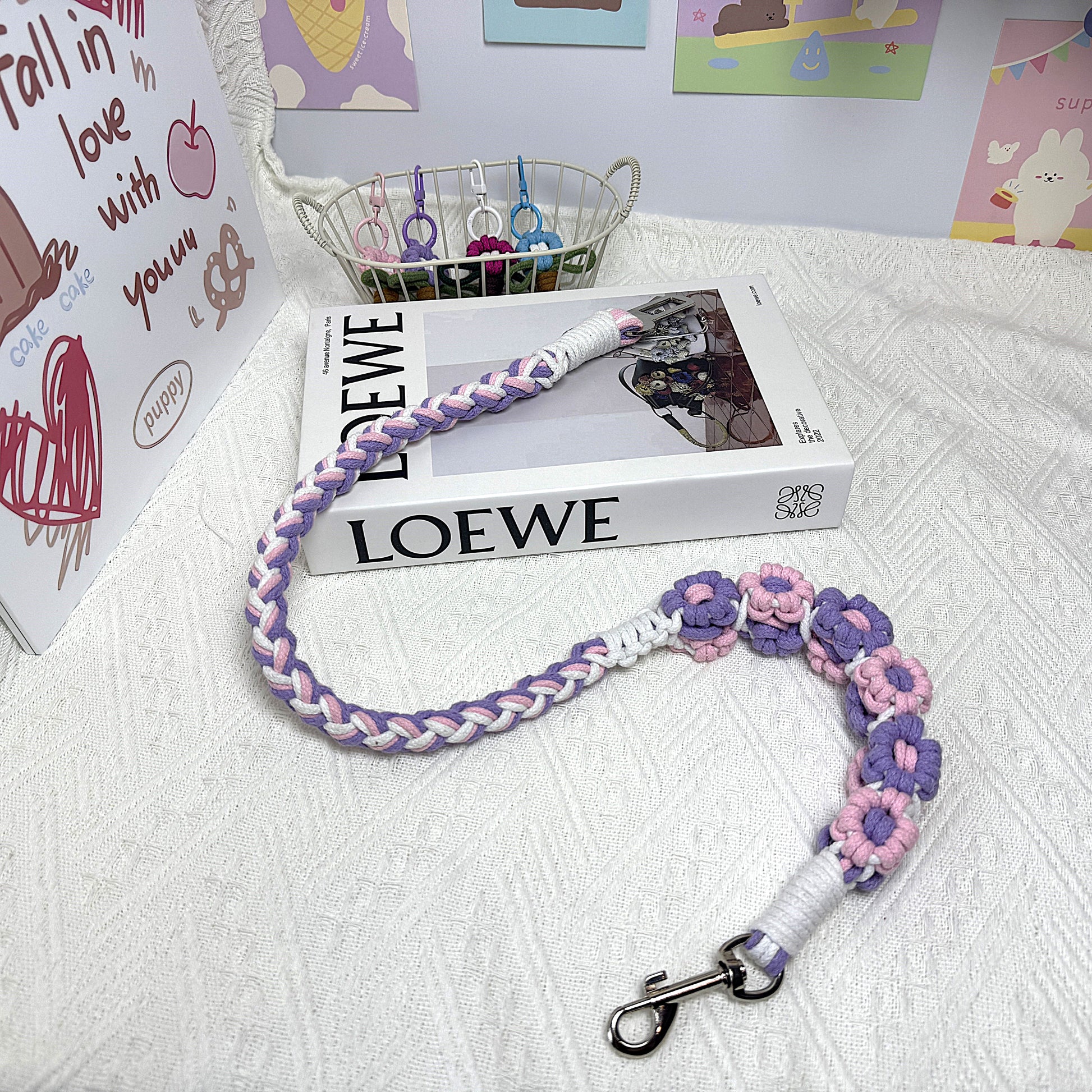A handwoven purple, pink, and white dog safety seatbelt displayed stylishly on a textured surface with floral details and a secure clasp, adding charm to pet accessories.