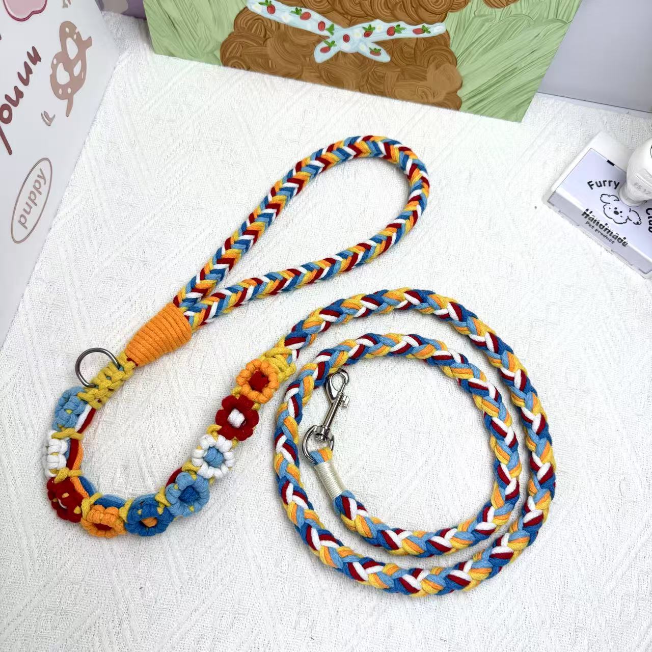 A handmade dog leash in red and blue with floral accents, featuring a metal clasp, placed on a textured white fabric background.