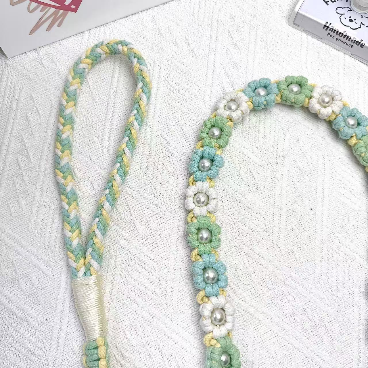 A detailed view of a mint green and yellow handwoven dog leash with a charming floral design. The leash is elegantly placed on a textured white surface, highlighting its intricate craftsmanship and vibrant colors.