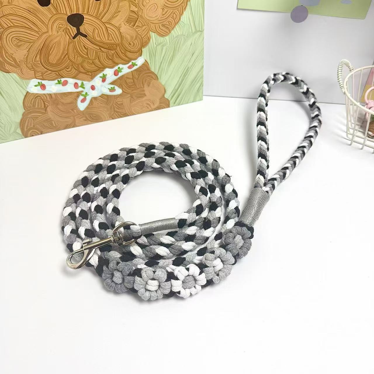 A handmade dog leash in black and gray with floral accents, featuring a metal clasp, placed on a textured white fabric background.