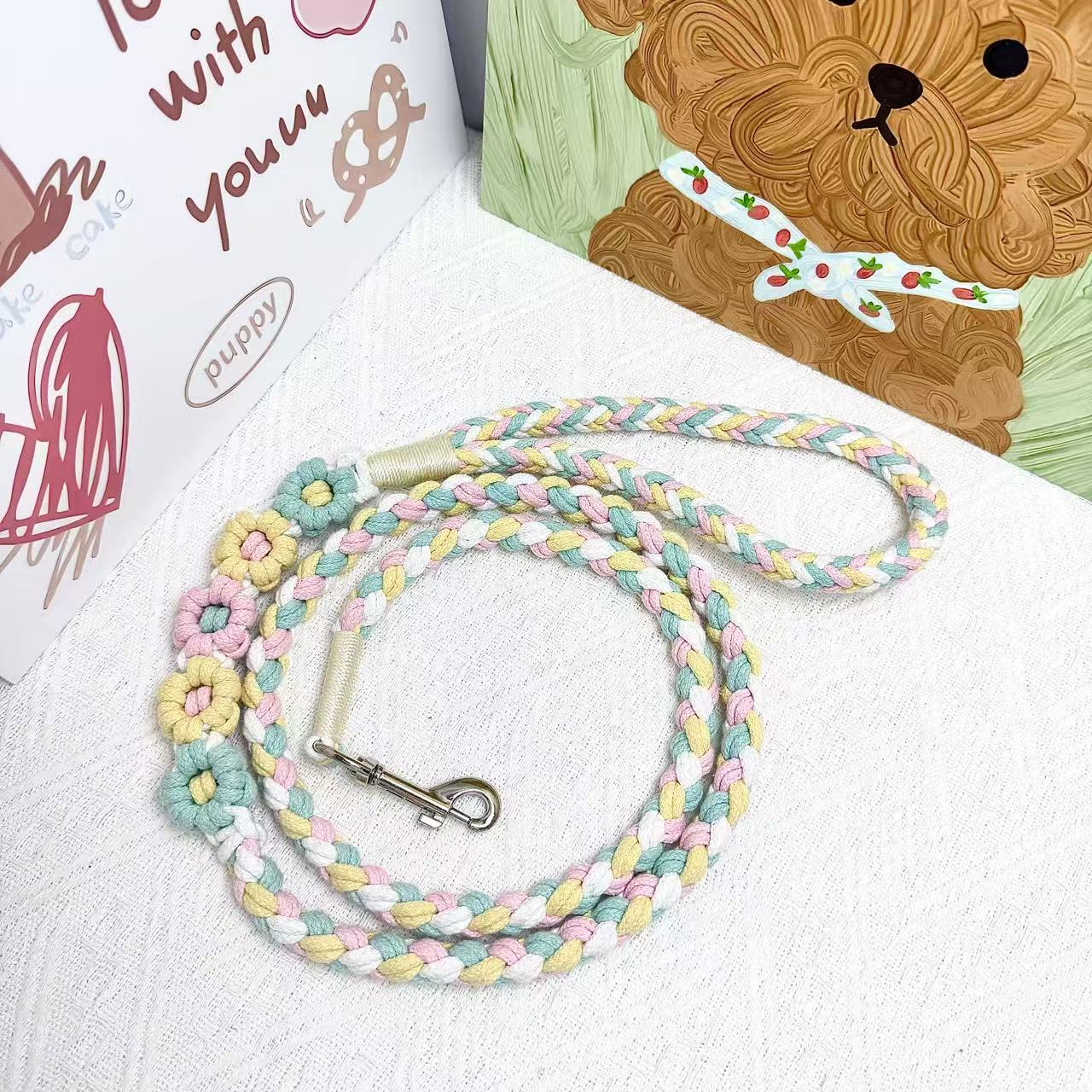 A handmade dog leash in blue and yellow with floral accents, featuring a metal clasp, placed on a textured white fabric background.