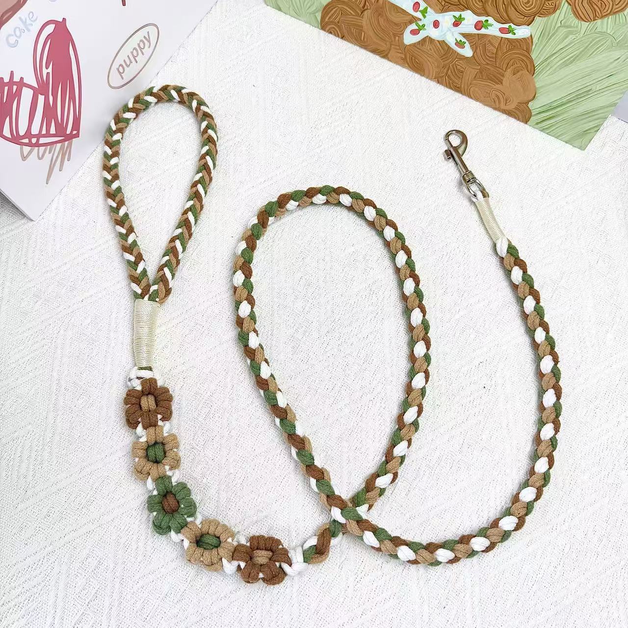 A handmade dog leash in green and brown with floral accents, featuring a metal clasp, placed on a textured white fabric background.