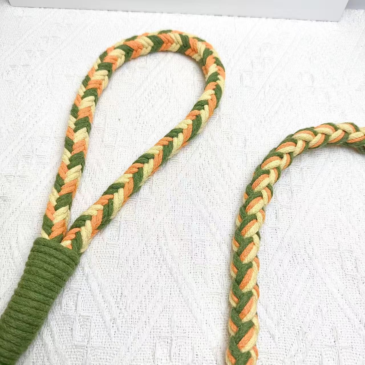 A detailed view of an orange, yellow, and green braided dog leash, highlighting its sturdy handwoven handle section and the neatly arranged leash cord.