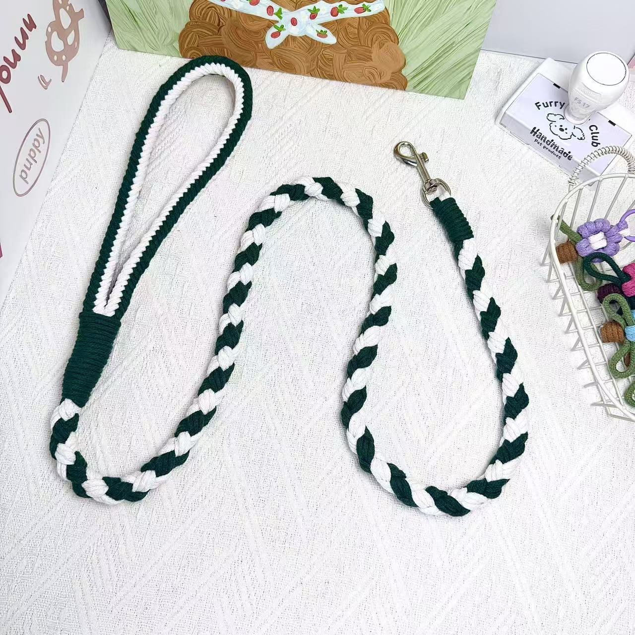 A handmade dog leash in cyan and white, featuring a metal clasp, placed on a textured white fabric background.