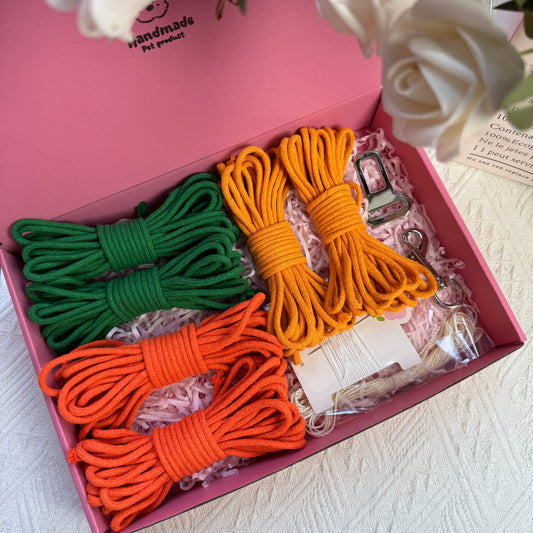 DIY dog car safety belt kit featuring green, orange, and yellow cotton ropes, one ice silk cord, one sewing kit, a metal buckle, and a metal clasp neatly arranged in a pink box with decorative shredded paper.