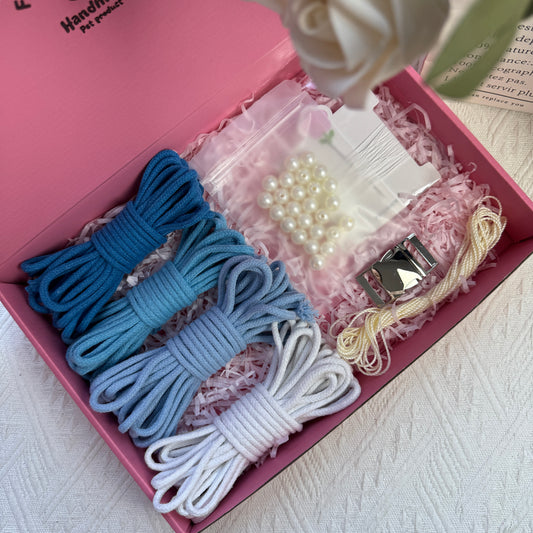 DIY dog collar kit featuring blue-toned cotton ropes, ice silk cord, a bag of pearls, one sewing kit, and a metal buckle, neatly arranged in a pink box with decorative shredded paper.