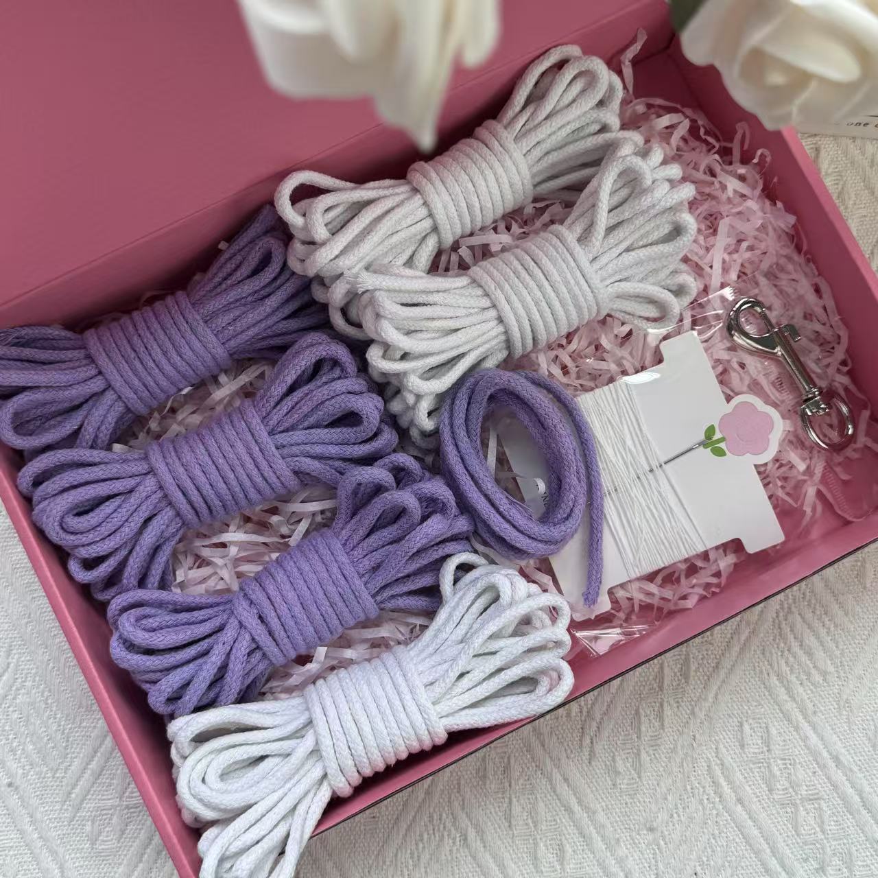 DIY dog leash kit featuring purple and white cotton ropes, one sewing kit, and a stainless steel clasp, neatly arranged in a pink box with decorative shredded paper.