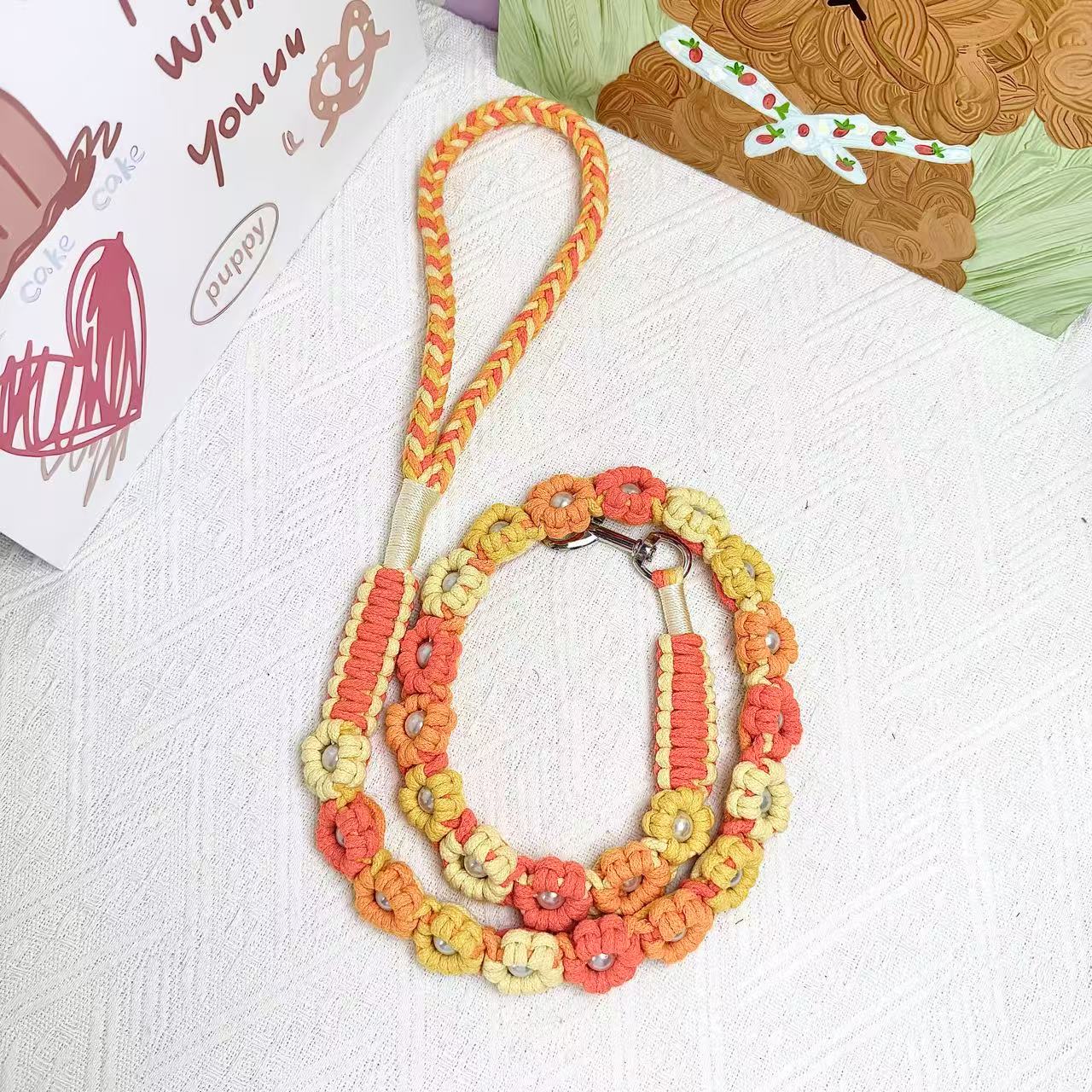 A handmade dog leash in gradient yellow with floral accents and pearl details, featuring a metal clasp, placed on a textured white fabric background.