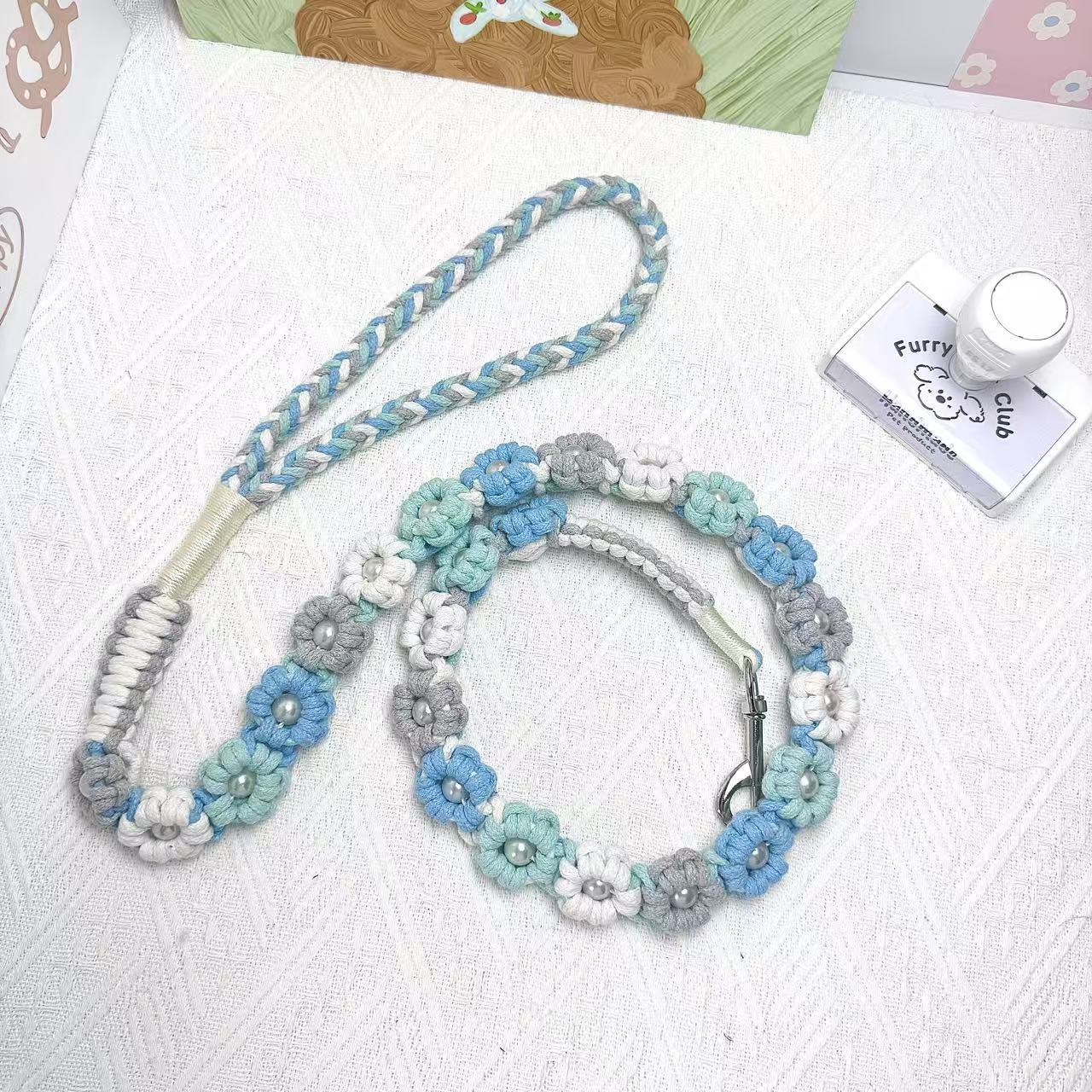 A handmade dog leash in ocean blue tones with floral accents and pearl details, featuring a metal clasp, placed on a textured white fabric background.