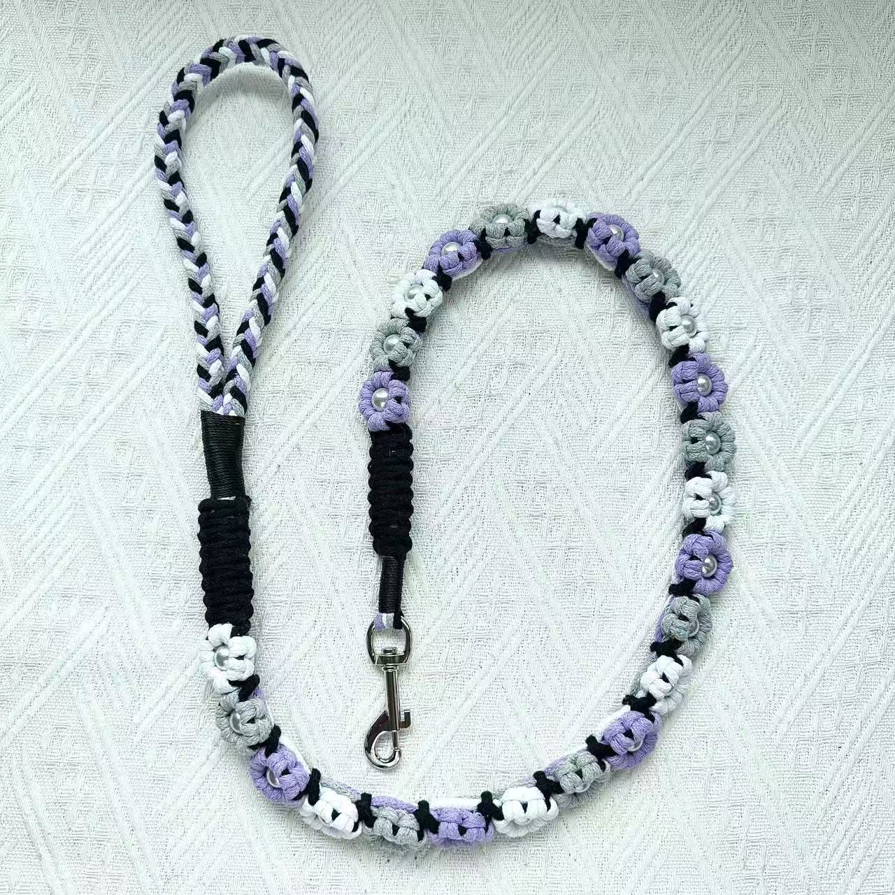 A handmade dog leash in purple and gray with floral accents and pearl details, featuring a metal clasp, placed on a textured white fabric background.
