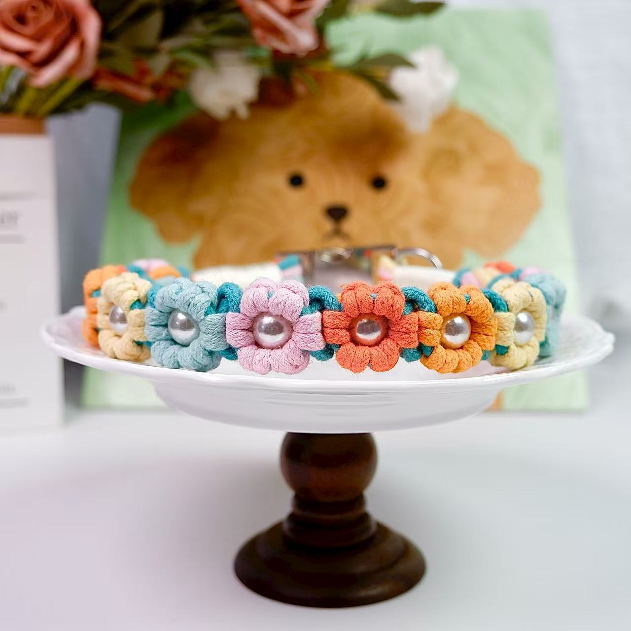 Colorful handmade dog collar with flower knots in orange, yellow, pink, red and blue, decorated with pearl centers, displayed on a white dish.